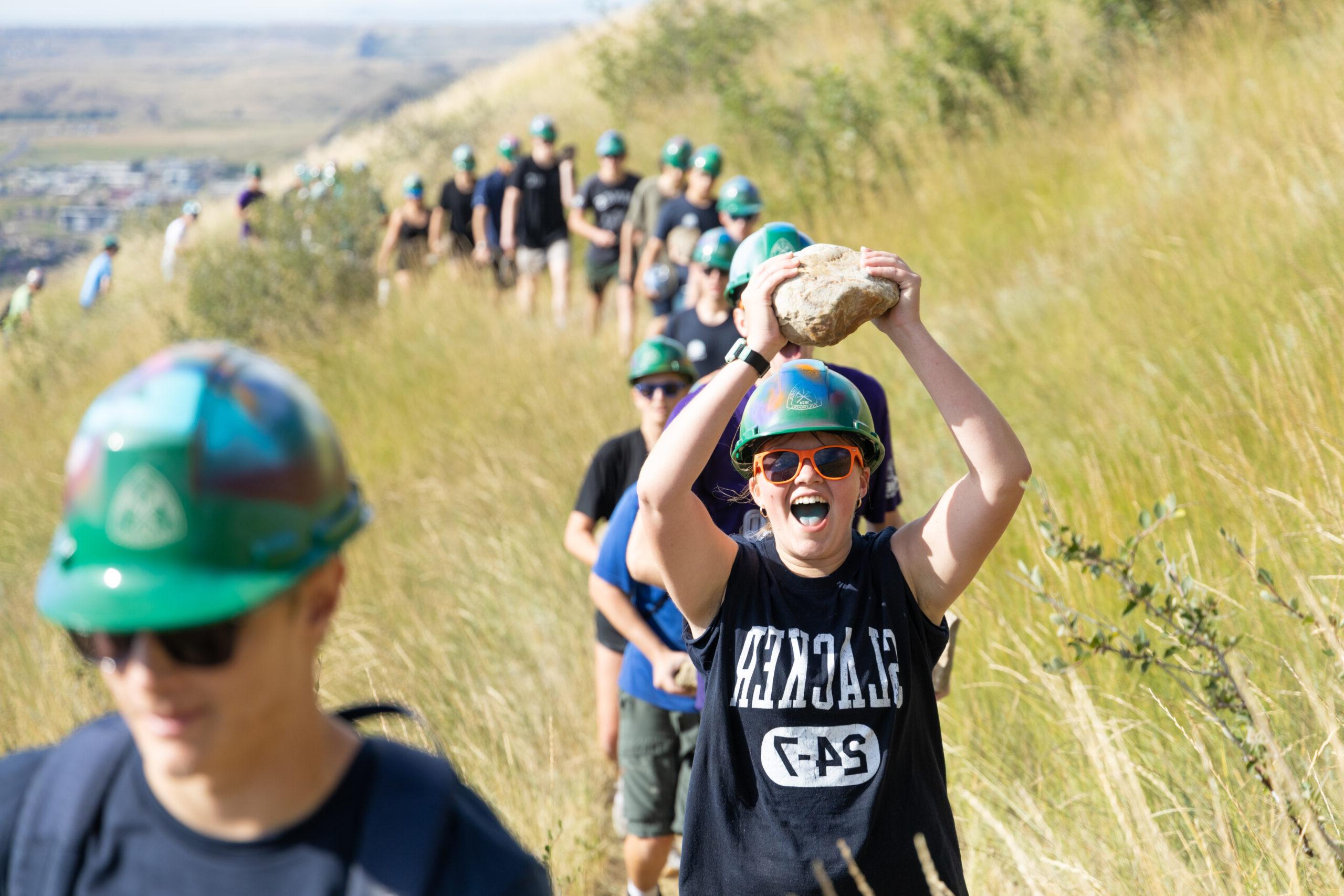 A student holds a rock above their head during the M Climb on Mt. Zion